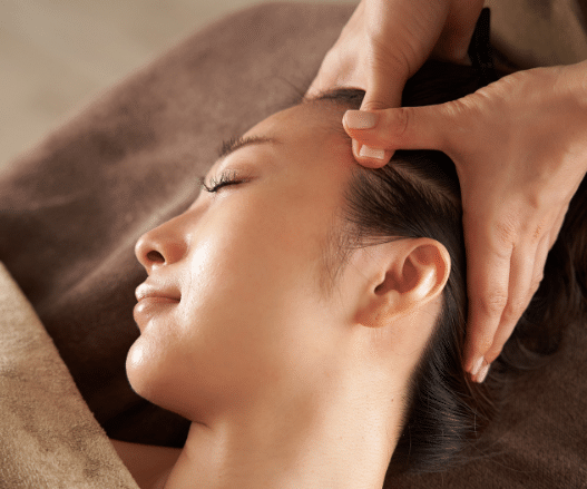 Lying comfortably on a towel-covered surface, eyes gently closed, the person relishes the soothing sensations of a head massage.