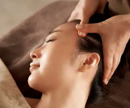 A person lies down at a World Cup Spa, receiving a head massage as hands gently press on the side of their scalp.