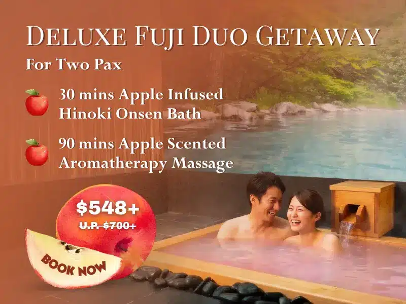 A smiling couple relax in an indoor wooden onsen bath. Promotional text offers a Fuji Apple-infused bath and apple-scented massage for two at £548+, down from £700+. Discover exclusive spa deals that let you unwind together in aromatic luxury.